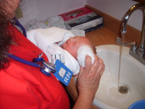 1989 Ford Bronco - A newborn baby is being bathed in a sink by a nurse wearing an RN badge and stethoscope.