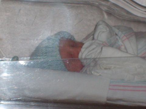 1989 Ford Bronco - A newborn baby is visible inside a clear incubator, swaddled in a blanket and wearing a cap.