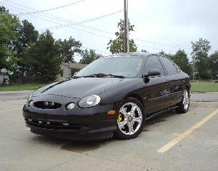 1997 Ford Taurus - A black 1997 Ford Taurus is parked in a lot on a cloudy day.