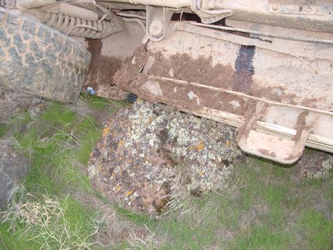 1989 Ford Bronco - A vehicle's undercarriage is lodged on a rock, covered in mud, with surrounding vegetation.