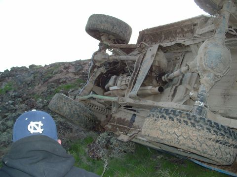 1989 Ford Bronco - An overturned SUV lies on its side in a landscape, its undercarriage exposed to the elements.