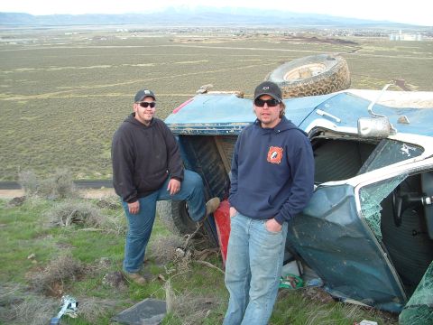 1989 Ford Bronco - This vehicle has been overturned in a rural landscape with two men posing beside it.