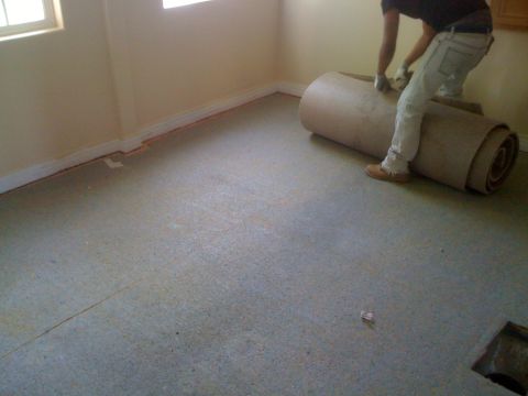 1968 Ford Mustang - Worker unrolling a carpet in a room with beige walls and a concrete floor.