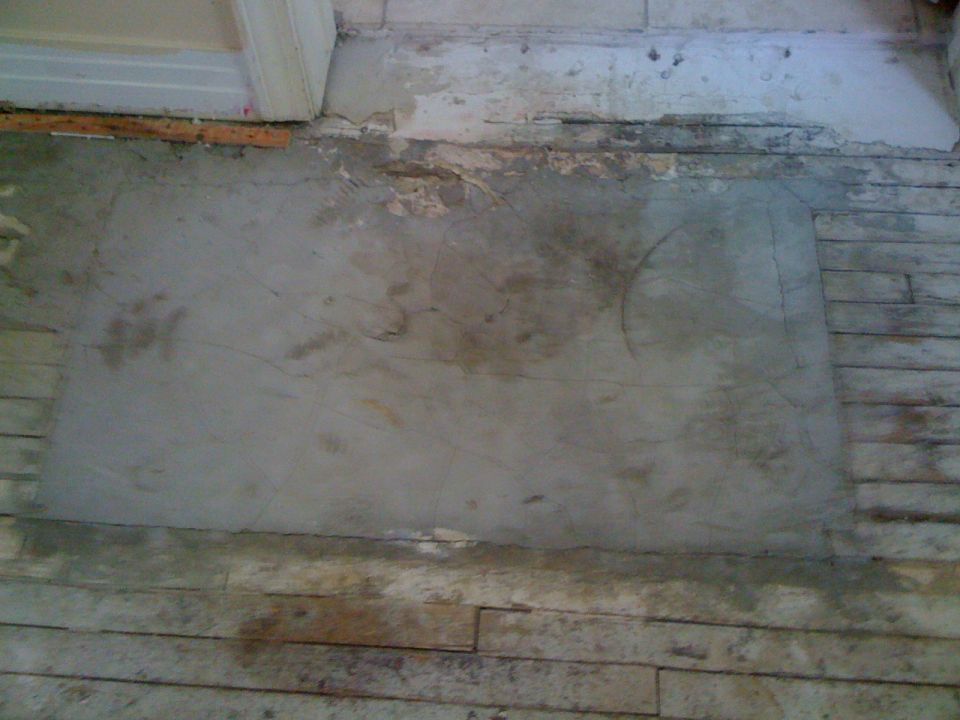 Interior floor with concrete patch and wooden planks, showing signs of disrepair