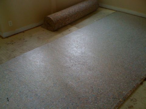 1968 Ford Mustang - Rolled carpet and flooring material are laid out on a subfloor in a room.