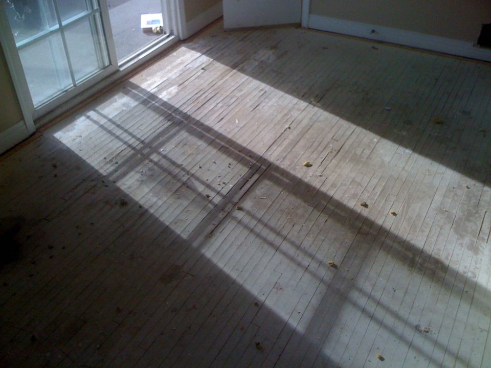 Interior scene of a room with a sliding glass door and worn wooden floorboards