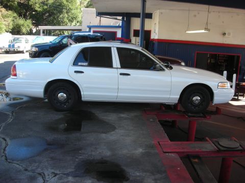 2004 Ford Crown Victoria - A white 2004 Ford Crown Victoria is positioned on a car lift in a service bay.