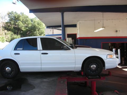 2004 Ford Crown Victoria - Side profile of a white 2004 Ford Crown Victoria, seen on a lift with a sticker on the rear window.
