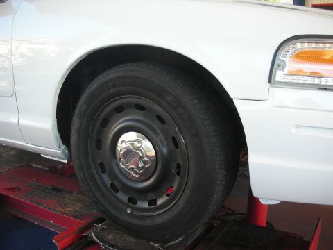 2004 Ford Crown Victoria - Front wheel and fender of a white 2004 Ford Crown Victoria on a lift.