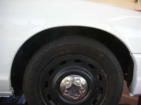 2004 Ford Crown Victoria - Close-up view of the front wheel well and tire on a white vehicle.