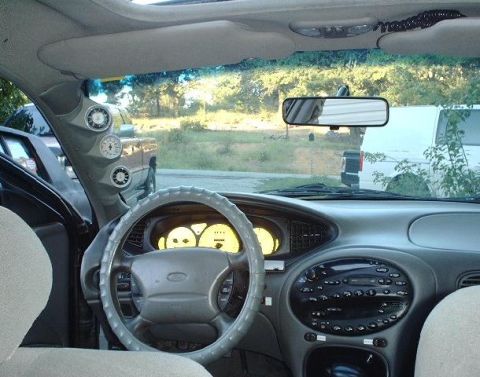 1997 Ford Taurus - Aftermarket gauges are mounted on the A-pillar of this car's interior, with other vehicles visible through the windshield.