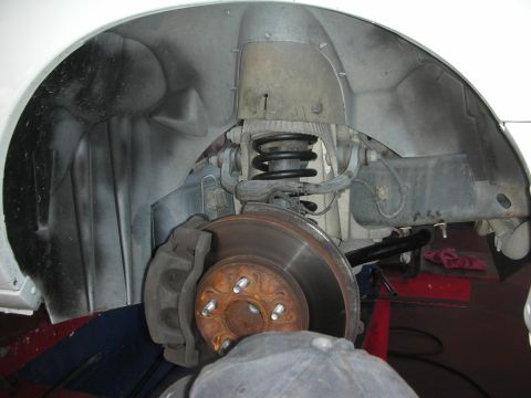 2004 Ford Crown Victoria - Close-up of a front suspension and brake assembly with the wheel removed, showing a rusty vented brake rotor, wheel hub with lug studs, bra…