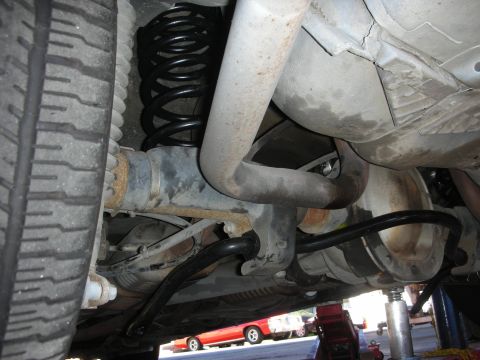 2004 Ford Crown Victoria - Underside view of a vehicle on a lift, showing rear suspension components including a black coil spring, sway bar, control arms, and exhaus…