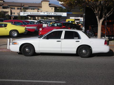 2004 Ford Crown Victoria - White Ford Crown Victoria sedan with steel wheels parked along a street outside Botkin Automotive and Bob's Alignment.