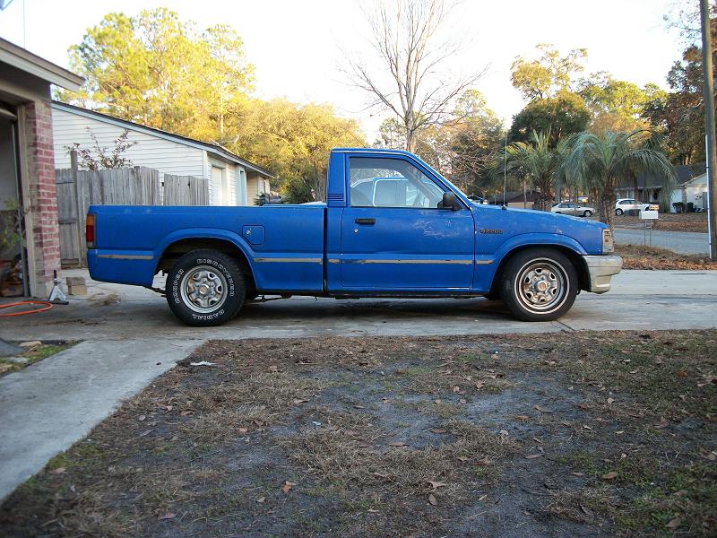 Blue Mazda single-cab pickup in side profile parked on grass by a driveway
