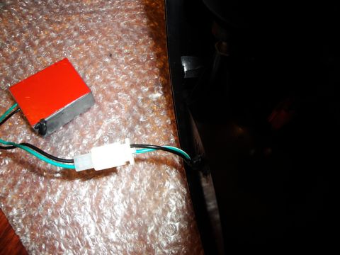 1993 Ford Taurus - A red electronic component with wires is shown connected to a dark car part, possibly a tail light assembly.