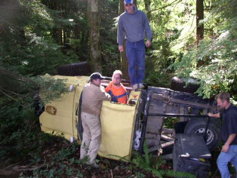 1979 Ford Bronco - Several people stand around a yellow truck that has overturned in a forest.