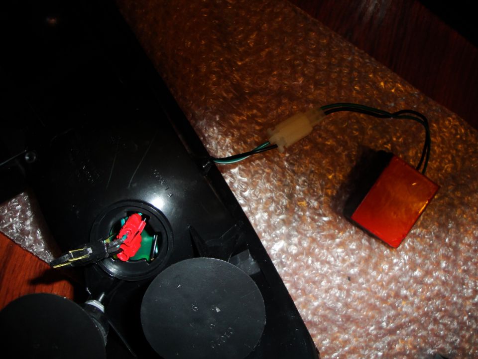 Close-up of a car tail light assembly with wiring and a small orange reflector