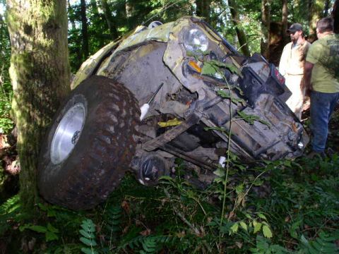 1979 Ford Bronco - A severely damaged off-road vehicle is wedged against a tree in a wooded area.