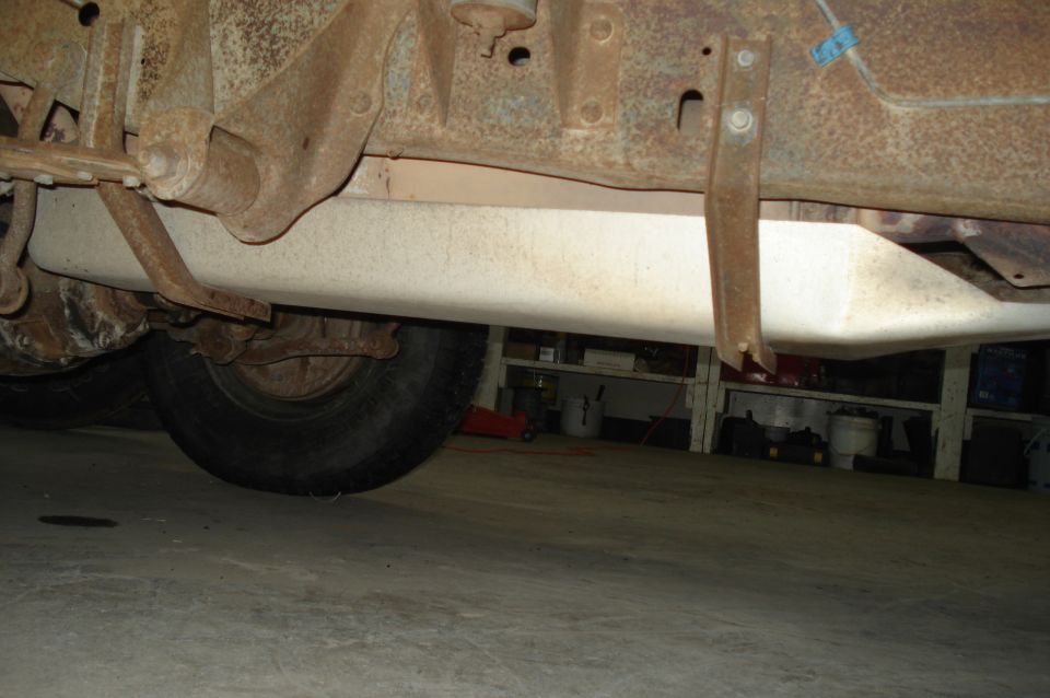 Undercarriage of a rusty vehicle showing a fuel tank and tire