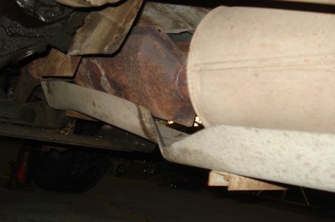 1979 Ford Bronco - The underside of a vehicle reveals a heavily rusted exhaust system and a tire supported by a jack.
