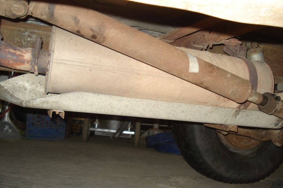 Underside view of a vehicle's exhaust muffler, driveshaft, and part of a tire
