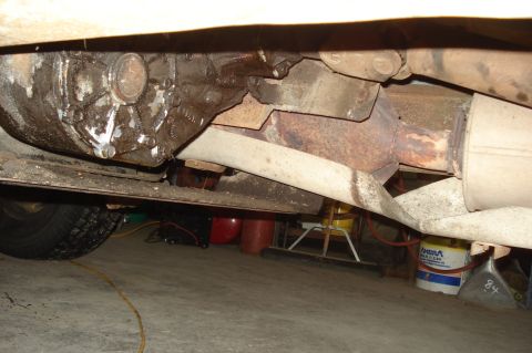 1979 Ford Bronco - The underside of a vehicle reveals its drivetrain components and exhaust system, with some signs of wear and tear.
