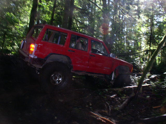 Red Jeep Cherokee XJ driving on a steep, wooded trail