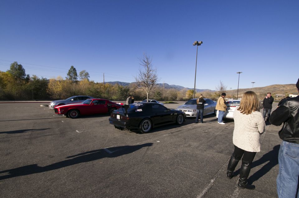 Black sports car with spoiler parked in a lot with other vehicles and people
