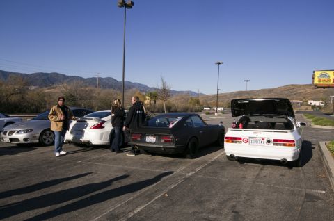 2006 Cadillac STS - Several cars are parked in a lot with people standing around them on a sunny day.