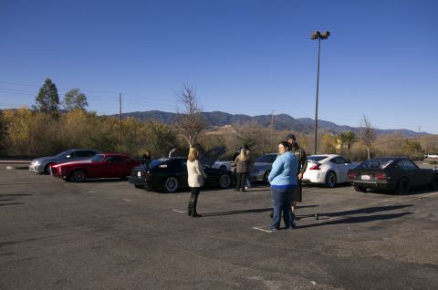 2006 Cadillac STS - People gather around various vehicles in an outdoor parking lot on a sunny day.