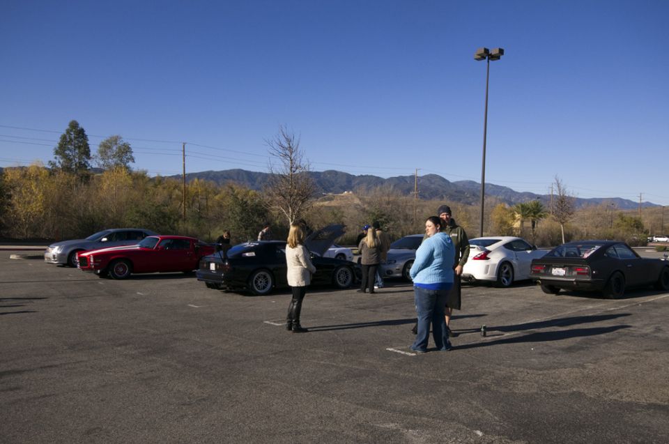 Several cars parked in a lot with people standing around, clear blue sky