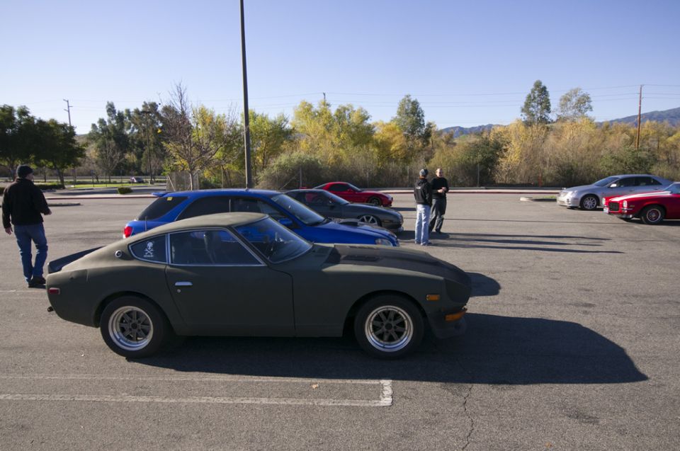 Dark green coupe, 3/4 front view, parked in a lot with other cars