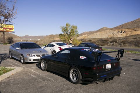 2006 Cadillac STS - Several sports cars are parked in a lot with mountains in the background.
