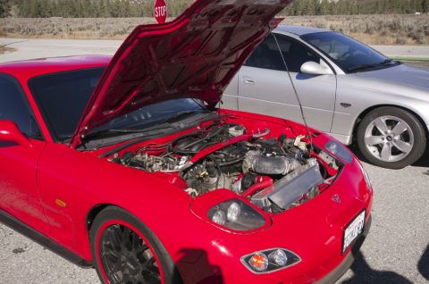 2006 Cadillac STS - A red sports car's engine is exposed while a silver sedan waits behind it.