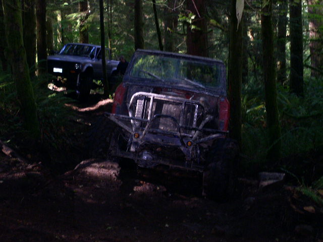 Off-road vehicle with custom bumper and exposed radiator, stuck in mud on a forest trail