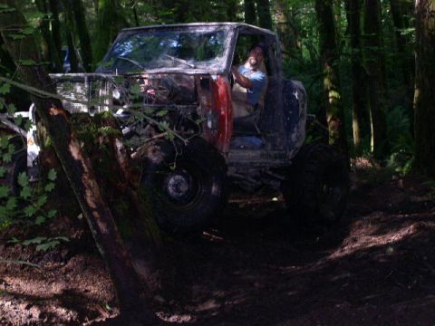 1979 Ford Bronco - A man drives a heavily modified off-road vehicle through a wooded area.