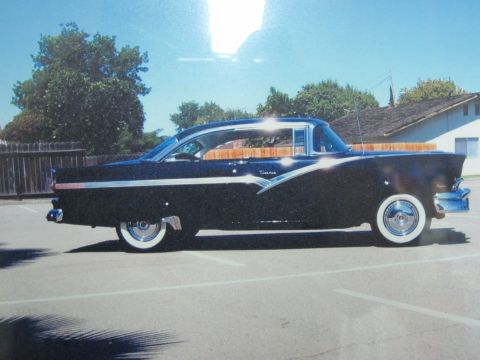 1956 Ford Fairlane - A black 1956 Ford Fairlane sedan is parked in a lot under a clear blue sky.
