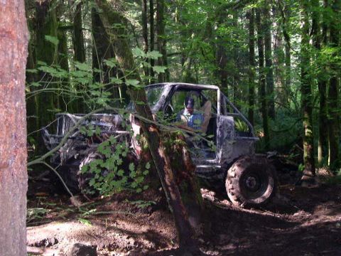 1979 Ford Bronco - A heavily modified off-road vehicle navigates a muddy trail through a dense forest.