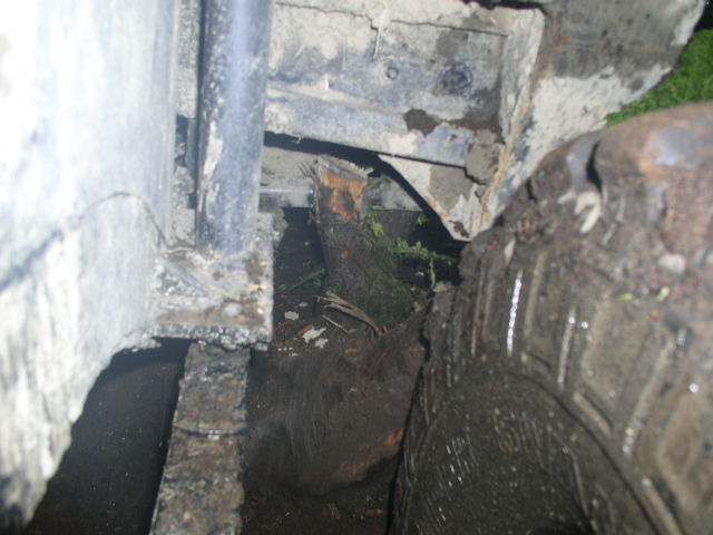 Close-up of a muddy wheel well and frame with a log lodged underneath