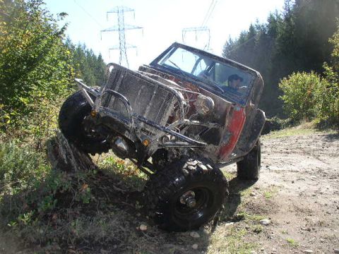 1979 Ford Bronco - Off-road vehicle navigating a rough dirt path with trees and power lines visible.