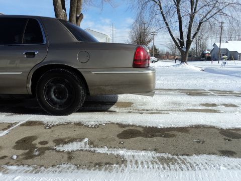 2004 Mercury Grand Marquis - Tan Mercury Grand Marquis rear quarter panel and steel wheel visible in a snowy environment.