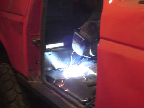 1989 Ford Bronco - Welding is performed on the floor of a red vehicle's interior.
