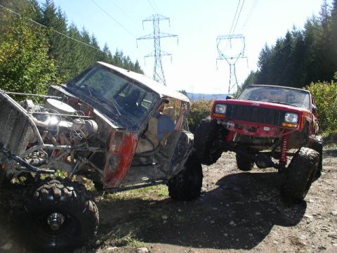 1979 Ford Bronco - Two modified off-road vehicles are navigating a muddy trail under power lines.