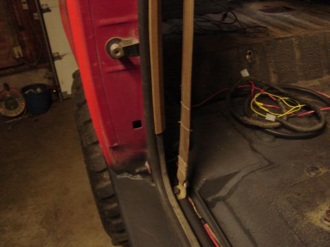 1989 Ford Bronco - Close-up of the interior of a red vehicle, showing the door jamb and floor with exposed wiring.