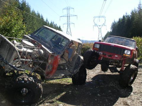 1979 Ford Bronco - Two heavily modified off-road vehicles are shown in a muddy outdoor setting with power lines overhead.