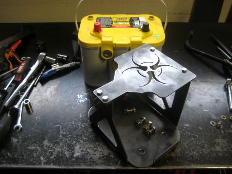 1996 Ford Bronco - A yellow top battery and a custom bracket with a biohazard symbol are shown on a workbench with tools.