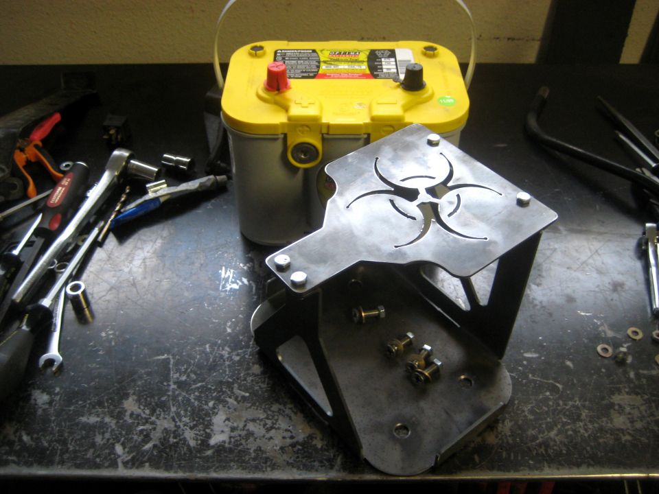 Yellow top battery next to a metal bracket with a biohazard symbol cut out. Tools are scattered around