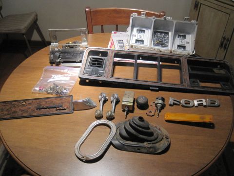 1979 Ford Bronco - Various interior parts, including a Ford emblem and dashboard trim, are laid out on a table.