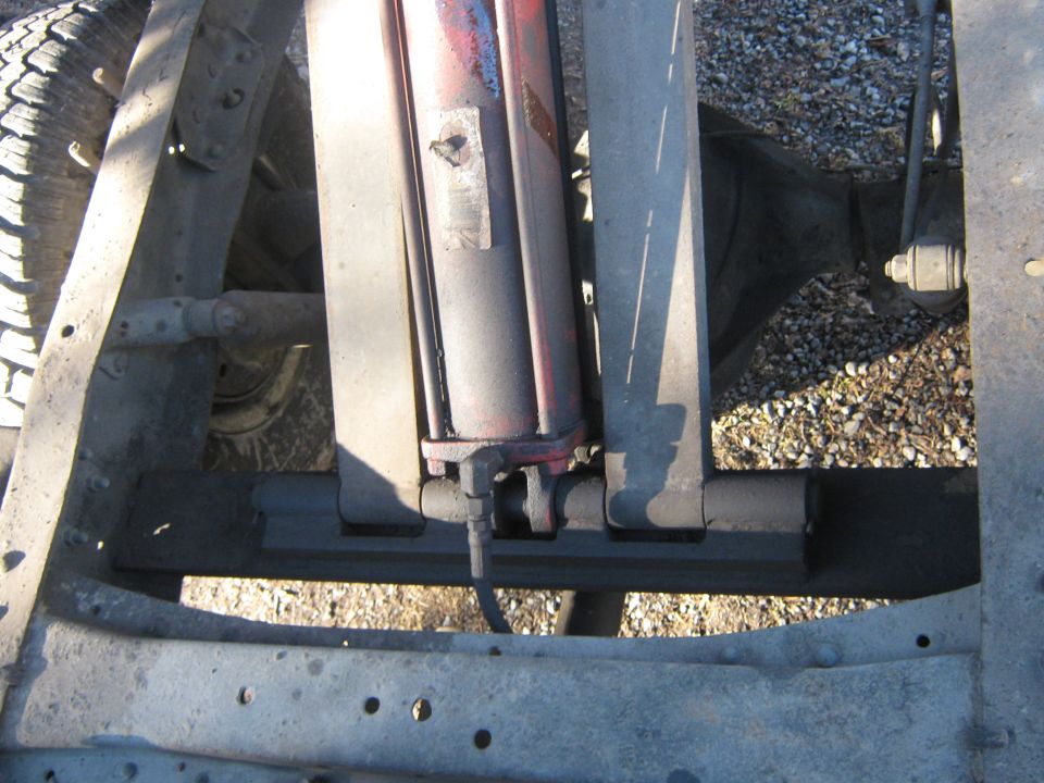 Close-up of a hydraulic cylinder mounted to a truck frame, with a tire visible